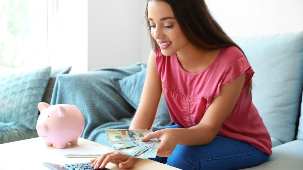 Happy Young Woman Using A Calculator And Holding Money