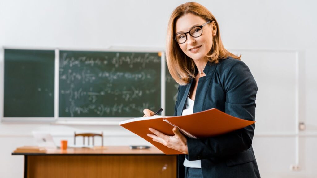 Woman Teaching Holding A File In Front Of A Blackboard