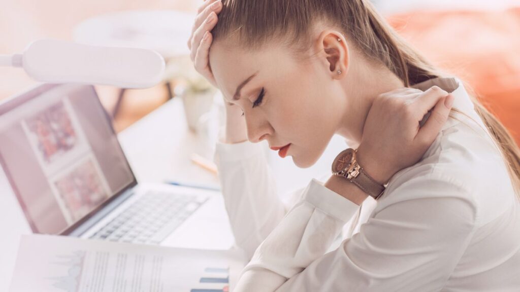 Woman Holding Her Head And Neck While Eyes Closed In Front Of Laptop
