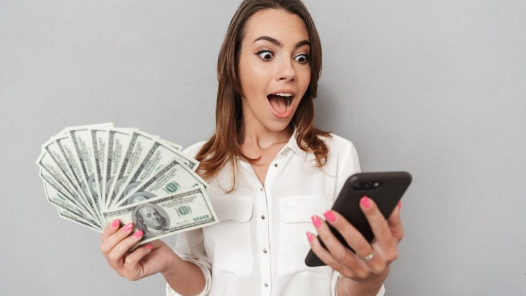 Shocked Woman Looking At Phone While Holding Money