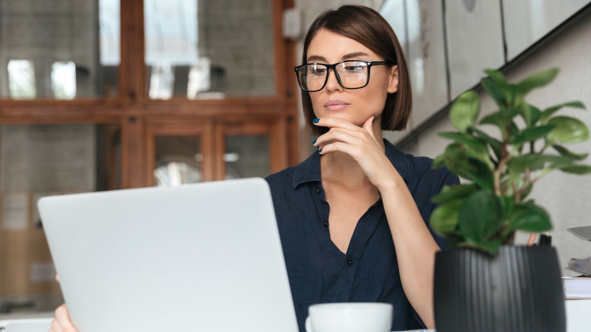 Short Haired Woman With Glasses Reading Using A Laptop