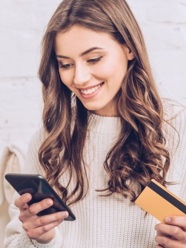 Young Woman Smiling While Looking At Phone And Holding A Card MSN