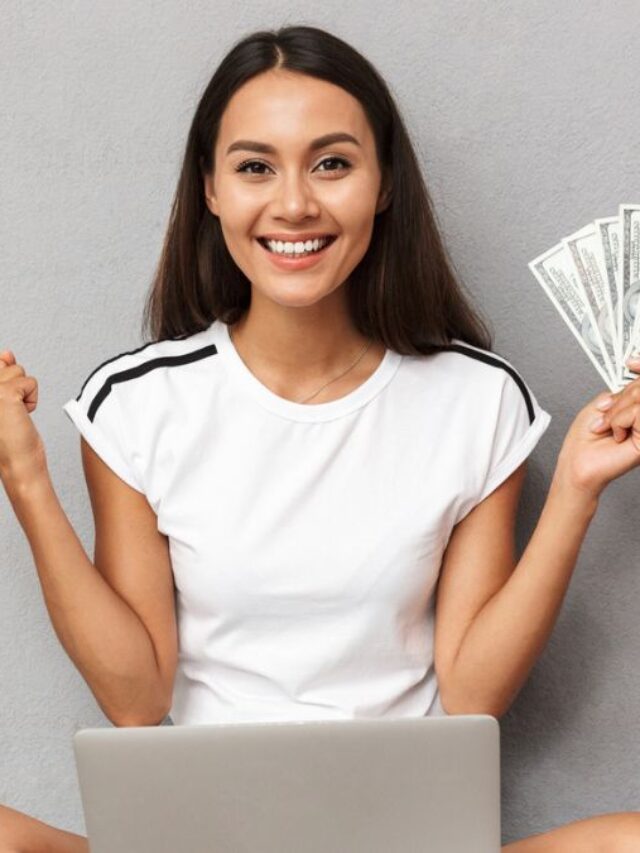 Happy Young Woman Sitting With Laptop On Her Lap Holding Cash Money