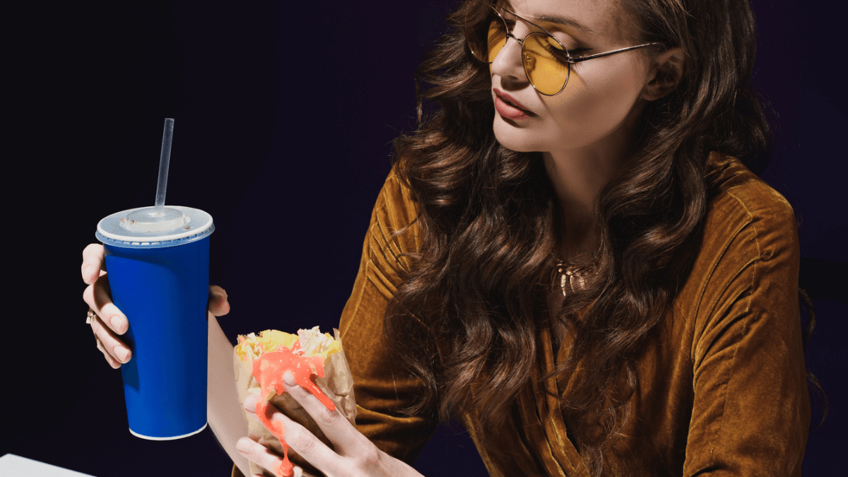 Woman with soda drink and shawarma wrap sitting at table