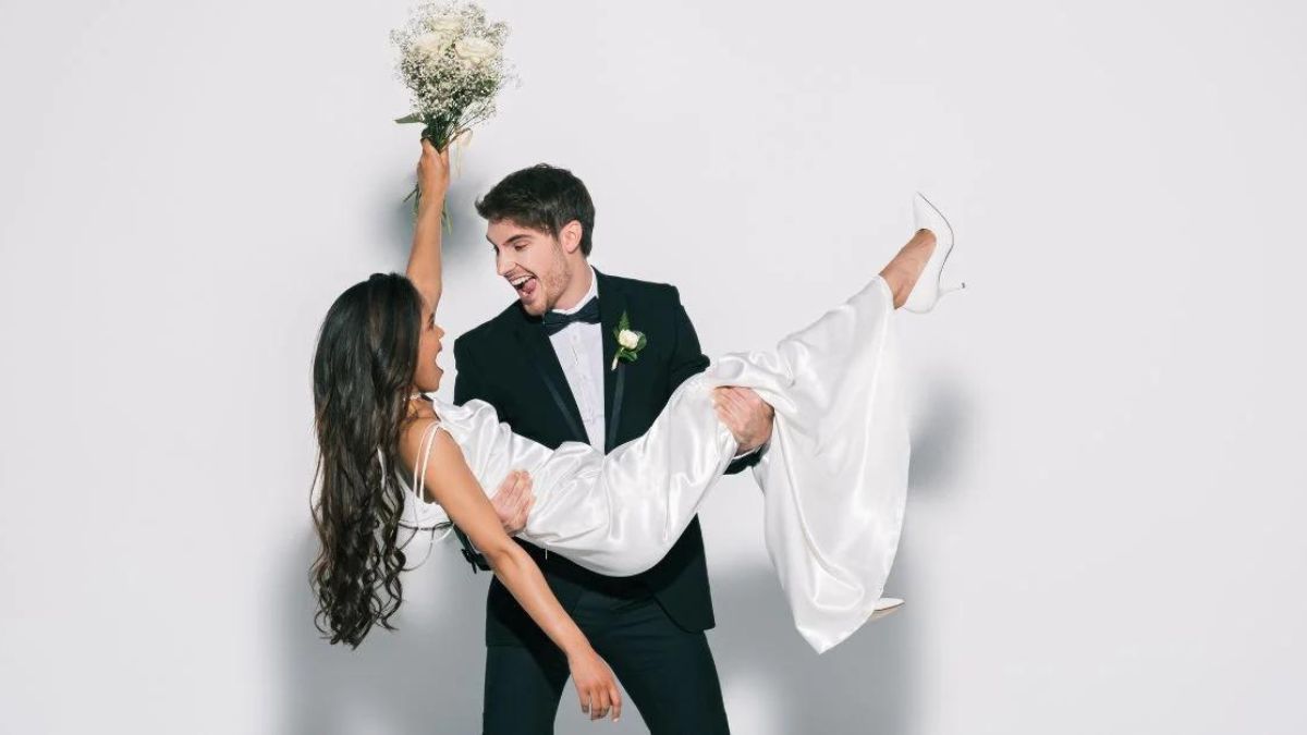 Man lifting his wife happily while she look at him with the same intensity while holding up her bouquet MSN