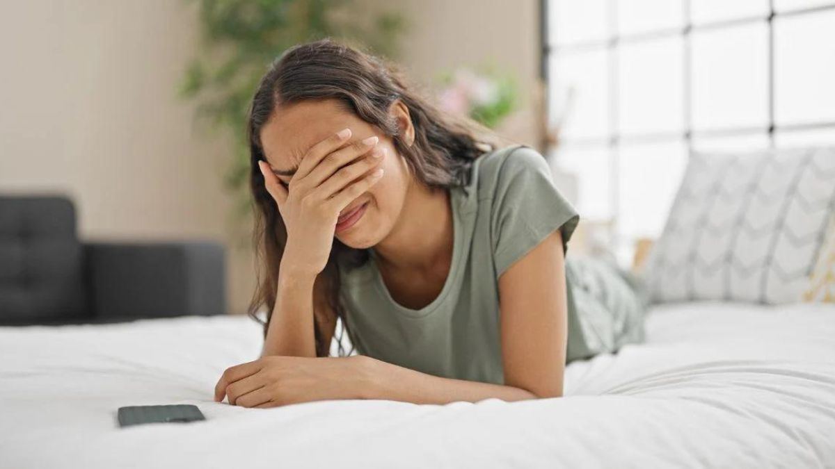 Woman in bed covering her eyes with one hand crying MSN