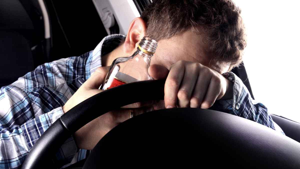 Man holding an alcohol bottle while leaning on the steering wheel MSN.