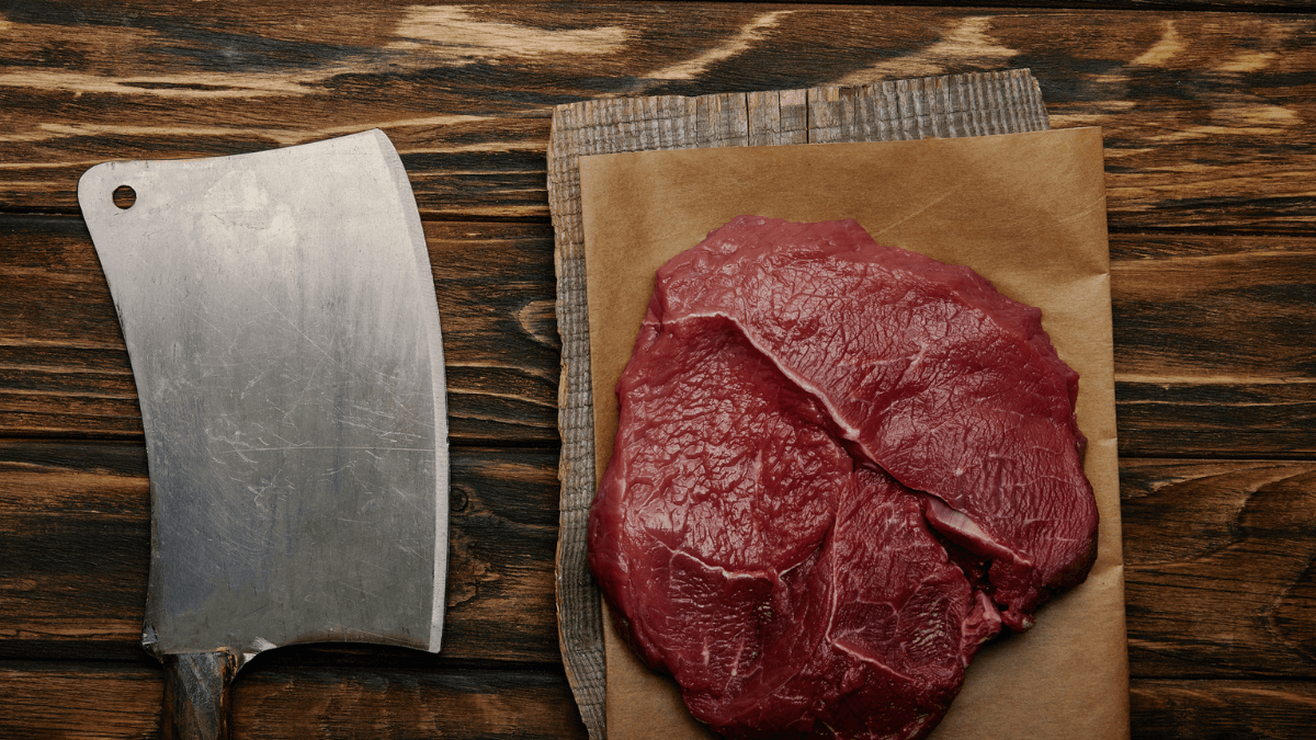 raw meat on baking paper with butcher knife